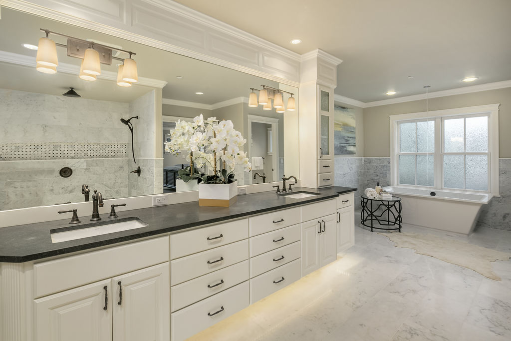 Modern double vanity design with white cabinets and storage featuring a black counter-top and marble flooring. Custom bathroom designed by Seattle architects specializing in home additions and remodels.