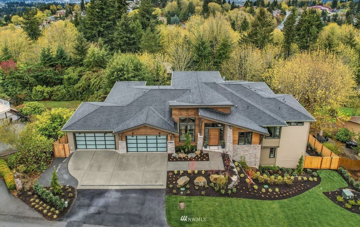 Aerial view of a modern two-story house with a gray roof, garage, large windows, and landscaped yard designed by Architectural Innovations, specializing in residential feasibility studies.