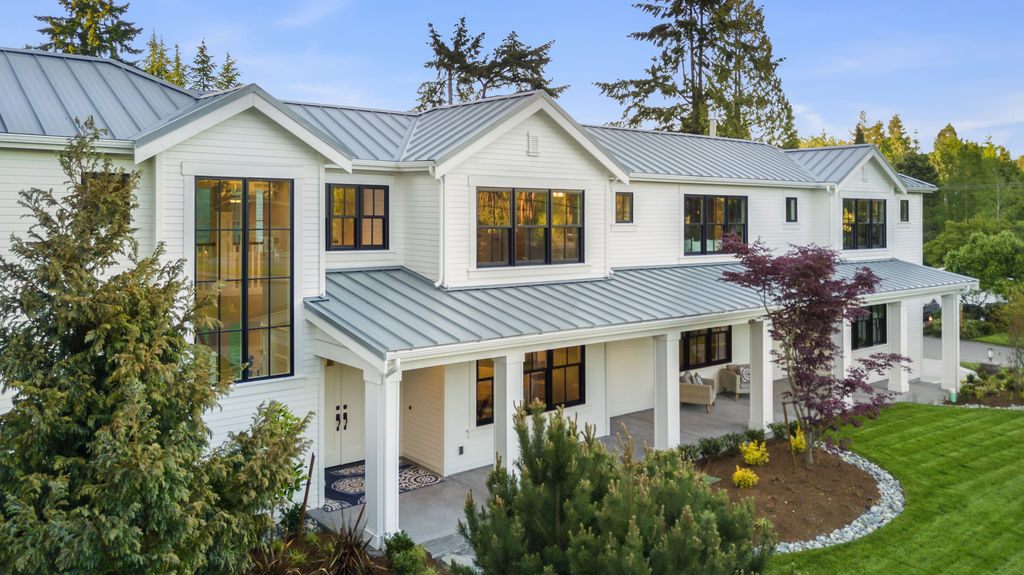 Modern two-story white farmhouse exterior in the Seattle area with front porch, large windows, and landscaping. Custom home floor plan design by Seattle architects from Architectural Innovations