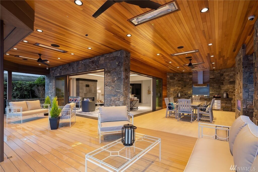 30.1725440_34_1 Spacious covered patio with wood ceiling, stone walls, and modern outdoor furniture—designed by a residential architect—with an open view into a stylish indoor living area and kitchen. Warm lighting creates a cozy, inviting atmosphere.