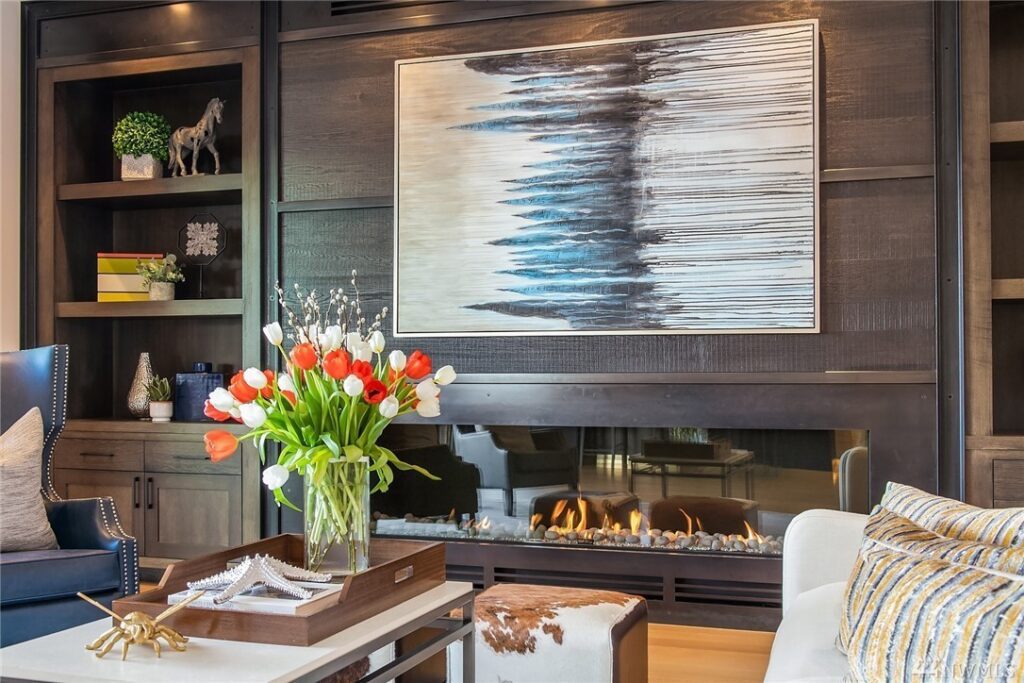 6.1725440_10_1 A modern living room by a residential architect features a glass vase with red and white tulips on a coffee table, a gas fireplace, abstract wall art, built-in shelves with books and decor, and a cozy, sophisticated ambiance.